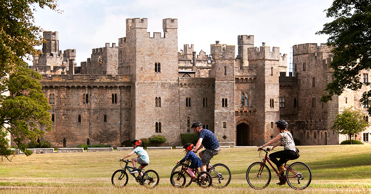 family riding past Raby Castle in the surrounding deer park